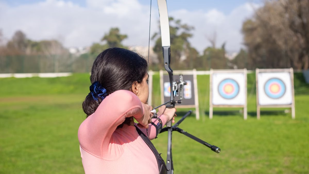 A woman aiming a bow and arrow at a target during outdoor archery practice.